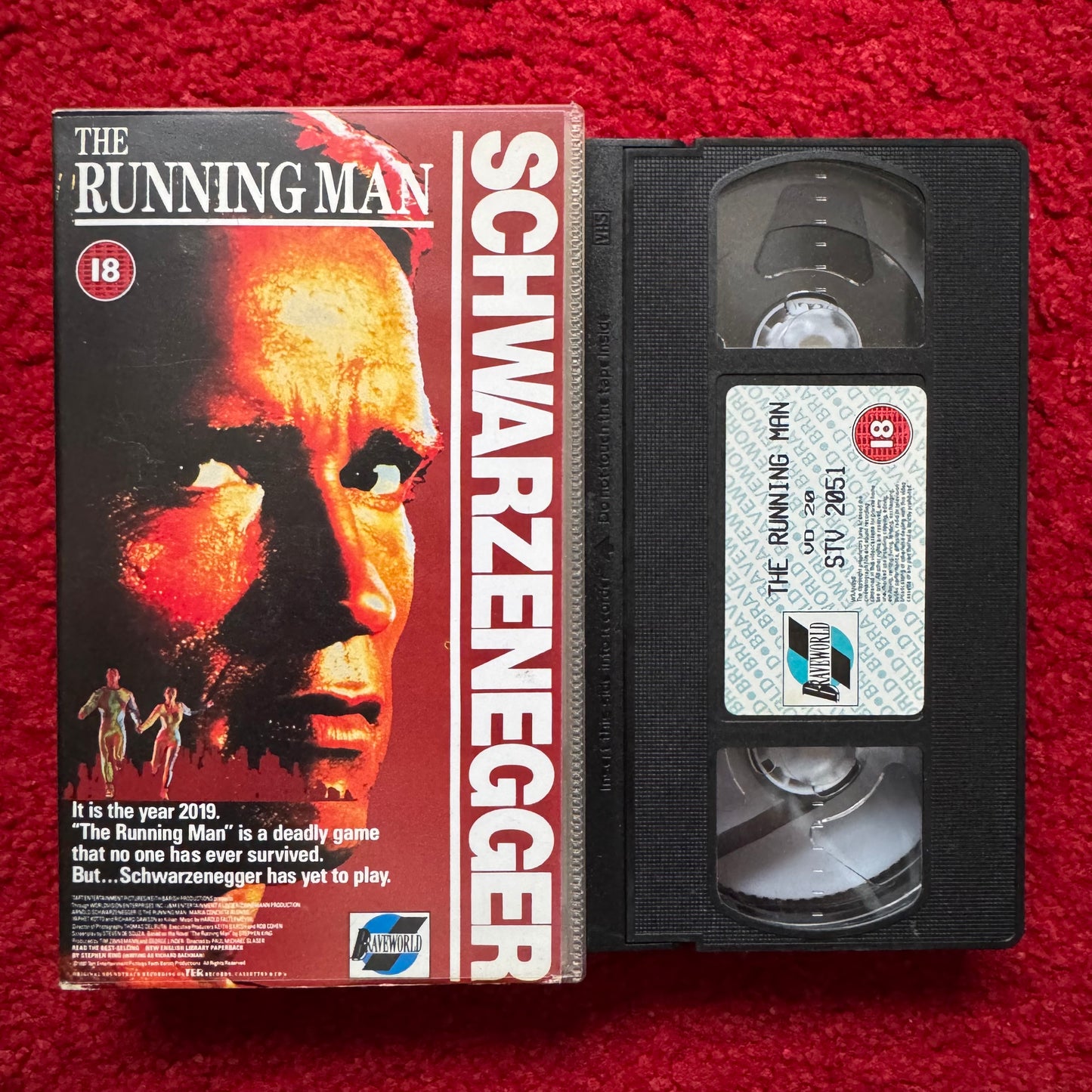 VHS tape of 'The Running Man' with cover on a red background