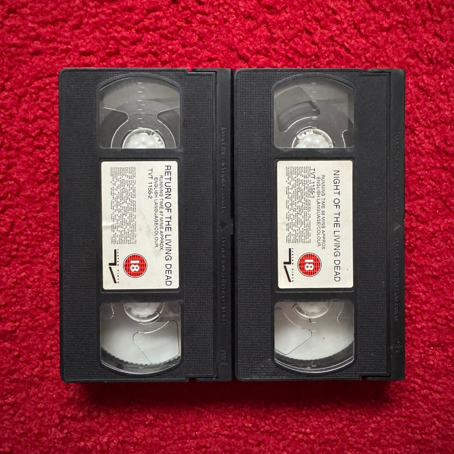 Two VHS tapes of 'Return of the Living Dead' and 'Night of the Living Dead' on a red background